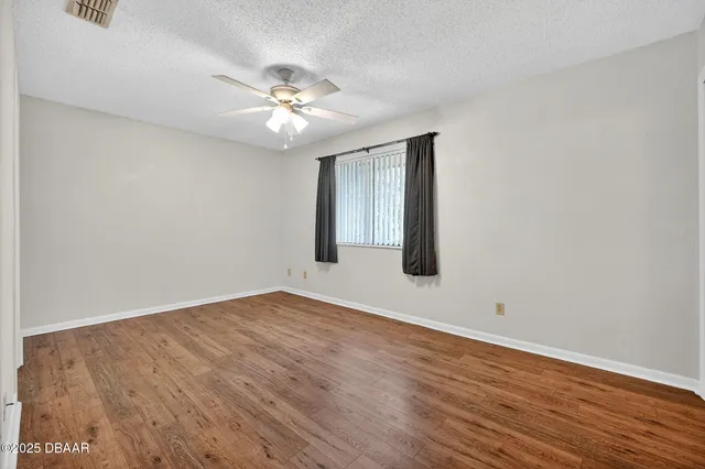 an empty room with wooden floor chandelier fan and windows