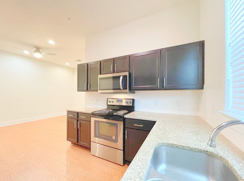 2400 Louis Henna Boulevard, Unit 103 Round Rock, TX 78664 - Photo 6 of 22 a kitchen with stainless steel appliances granite countertop a sink and a stove top oven with wooden floor