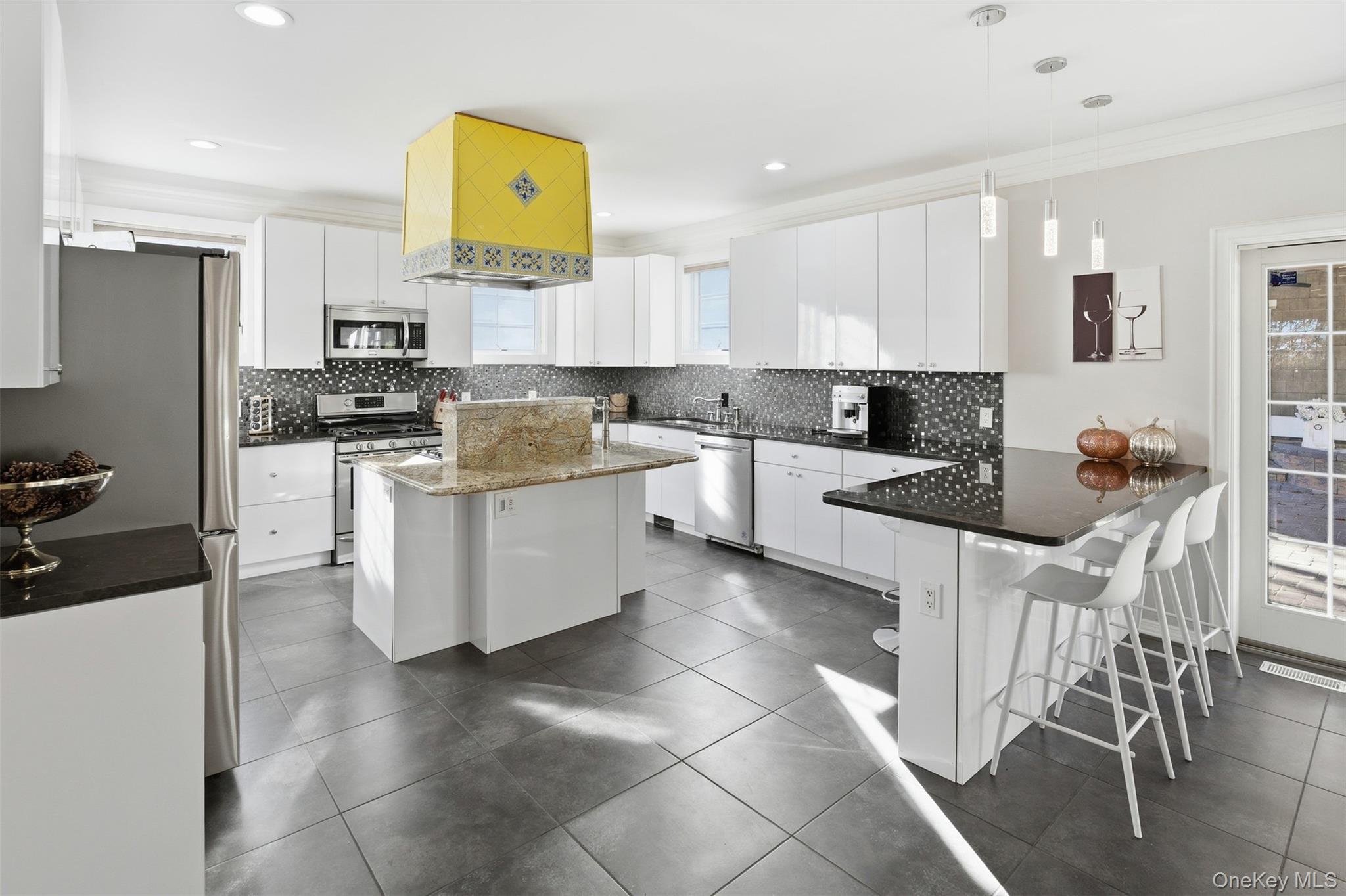 33 A Newtown Road Hampton Bays, NY 11946 - Photo 23 of 50 Kitchen featuring white cabinets, appliances with stainless steel finishes, decorative light fixtures, a kitchen breakfast bar, and dark stone counters