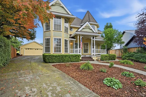 a view of a white house next to a yard with plants and trees