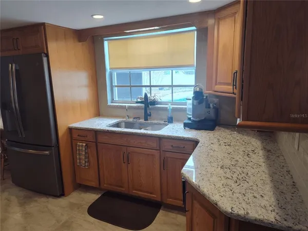 a kitchen with granite countertop wooden cabinets a refrigerator a sink and a window