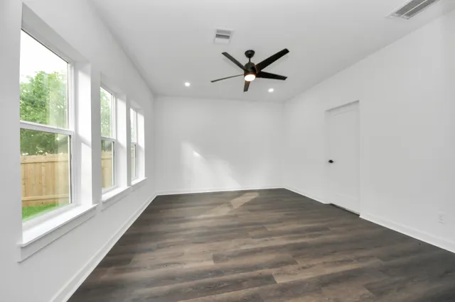 an empty room with wooden floor fan and windows