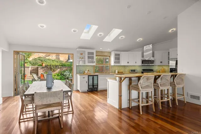 a living room with stainless steel appliances furniture a dining table wooden floor and kitchen view