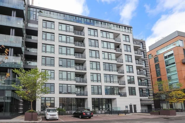 a front view of a building with lot of cars and trees