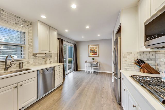 a kitchen with stainless steel appliances granite countertop a stove top oven a sink dishwasher and white cabinets with wooden floor