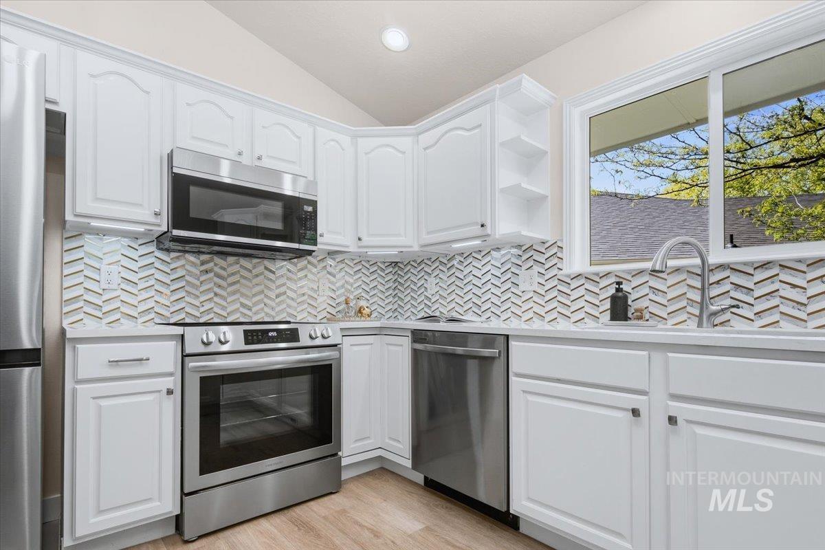 725 North Eagle Road Eagle, ID 83616 - Photo 10 of 45 Kitchen featuring white cabinetry, stainless steel appliances, a chevron pattern tile backsplash, light-toned countertops, and wood-finish flooring
