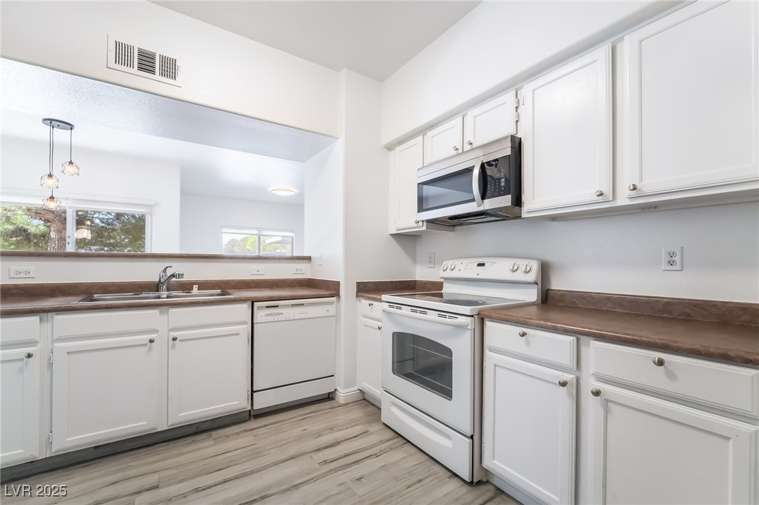 7255 West Sunset Road, Unit 1148 Las Vegas, NV 89113 - Photo 17 of 62 Kitchen featuring white appliances, dark countertops, white cabinetry, light wood-style floors, and hanging light fixtures