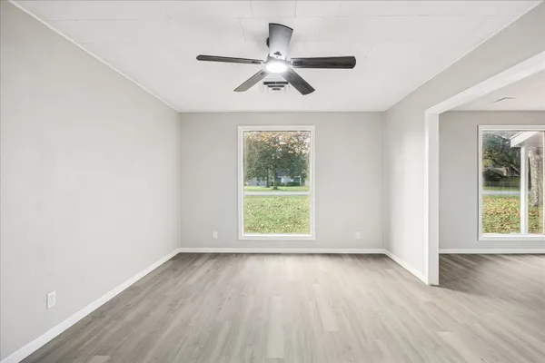an empty room with wooden floor chandelier fan and windows