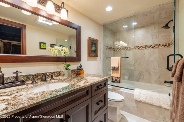 a bathroom with a granite countertop sink a toilet a mirror and shower