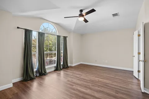 an empty room with wooden floor fan and windows
