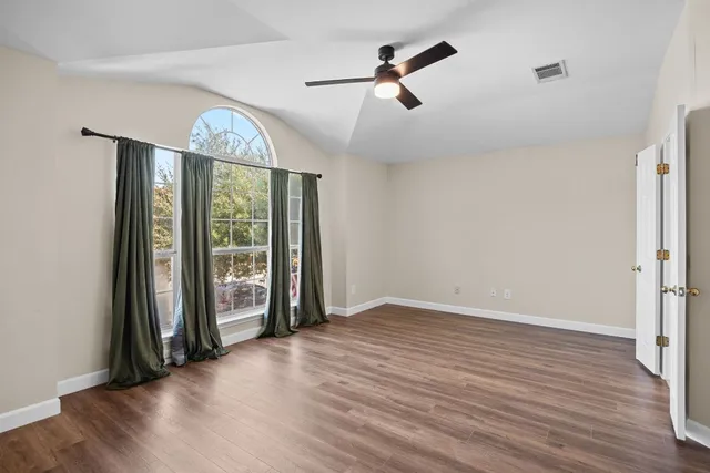 an empty room with wooden floor fan and windows