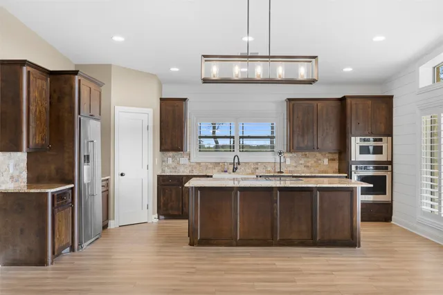 a kitchen with stainless steel appliances granite countertop a refrigerator a sink dishwasher a stove and a dining table with wooden floor