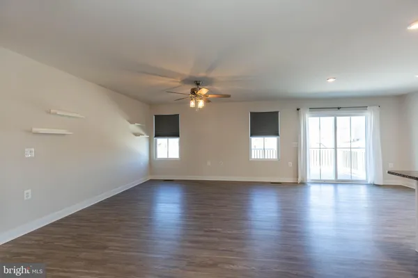 a view of an empty room with wooden floor and fan