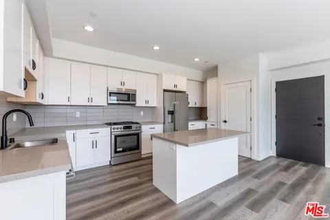 a kitchen with stainless steel appliances granite countertop a stove top oven a sink a refrigerator and white cabinets with wooden floor