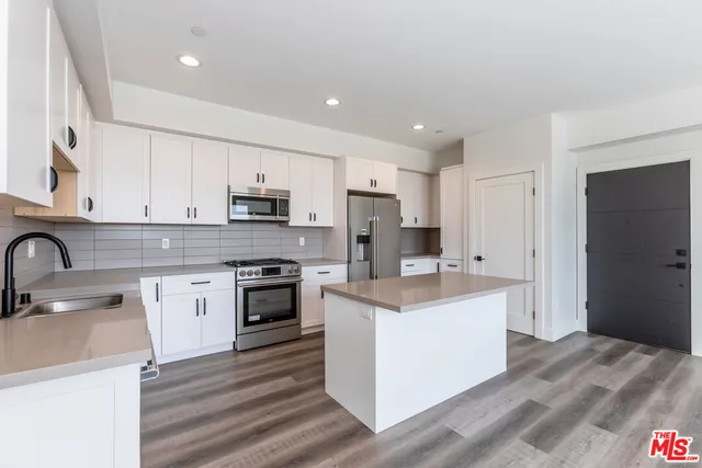 a kitchen with stainless steel appliances granite countertop a stove top oven a sink a refrigerator and white cabinets with wooden floor