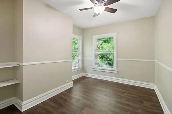 an empty room with wooden floor fan and windows