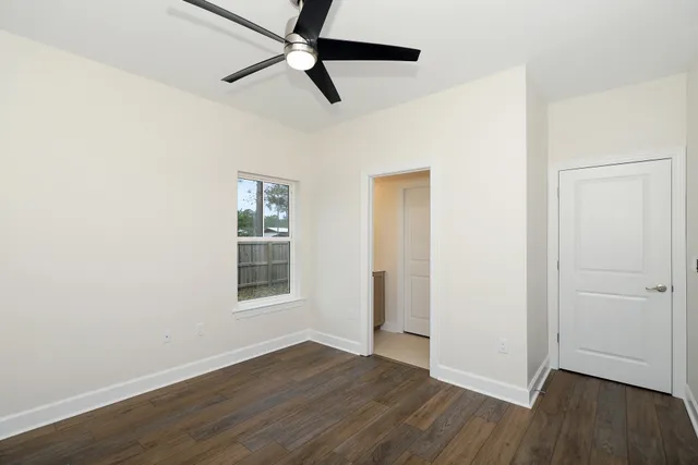 an empty room with wooden floor ceiling fan and windows