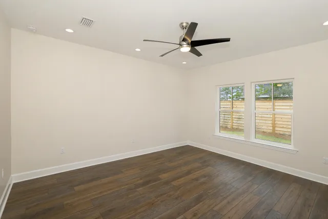 an empty room with wooden floor fan and windows