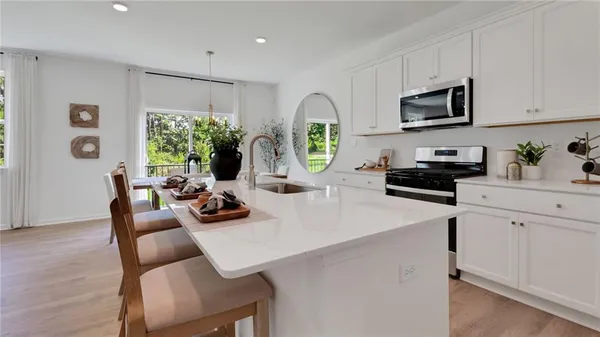 a kitchen with stainless steel appliances a microwave a stove a refrigerator a sink a dining table and chairs with wooden floor