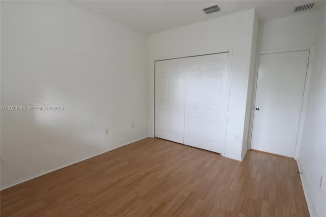 a view of an empty room with wooden floor and closet area