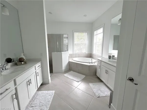 a large white bathroom with a double vanity sink a mirror and a bathtub