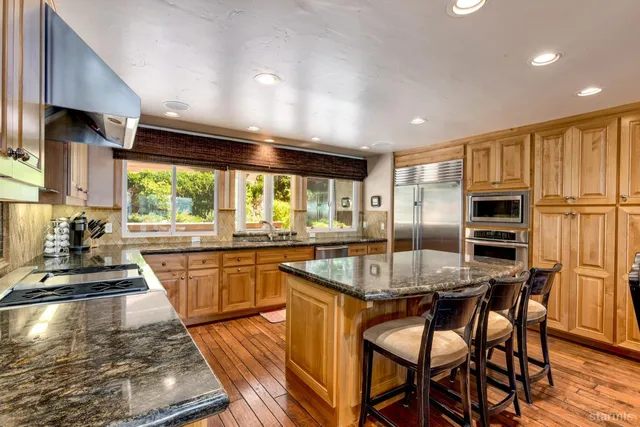 a kitchen with stainless steel appliances granite countertop a stove top oven a sink a dining table and chairs with wooden floor