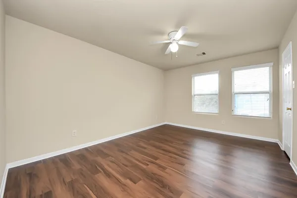 an empty room with wooden floor fan and windows