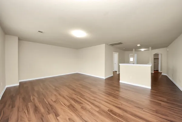 a view of an empty room with wooden floor and a kitchen