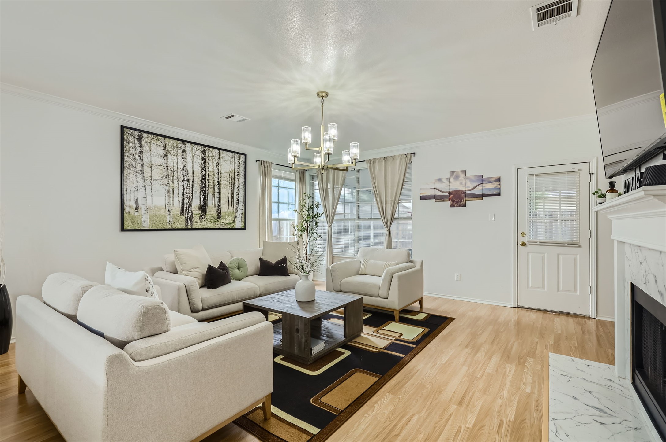 1016 Thackeray Lane Pflugerville, TX 78660 - Photo 4 of 28 Living room with crown molding, a high end fireplace, light wood-style flooring, and a chandelier