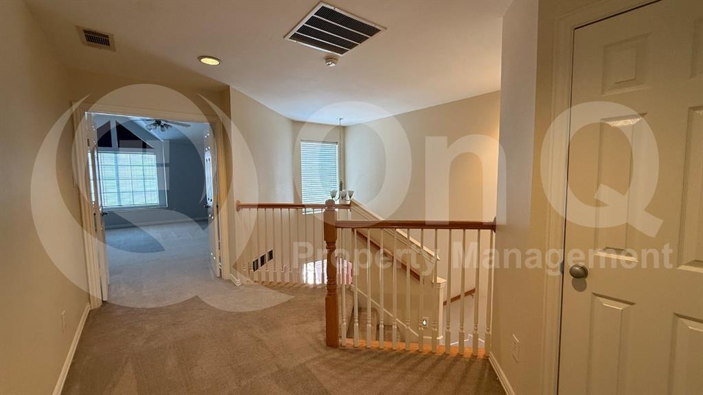 18240 Midway Road, Unit 1204 Dallas, TX 75287 - Photo 18 of 27 Carpeted hallway with painted walls, featuring a wooden handrail and white balusters