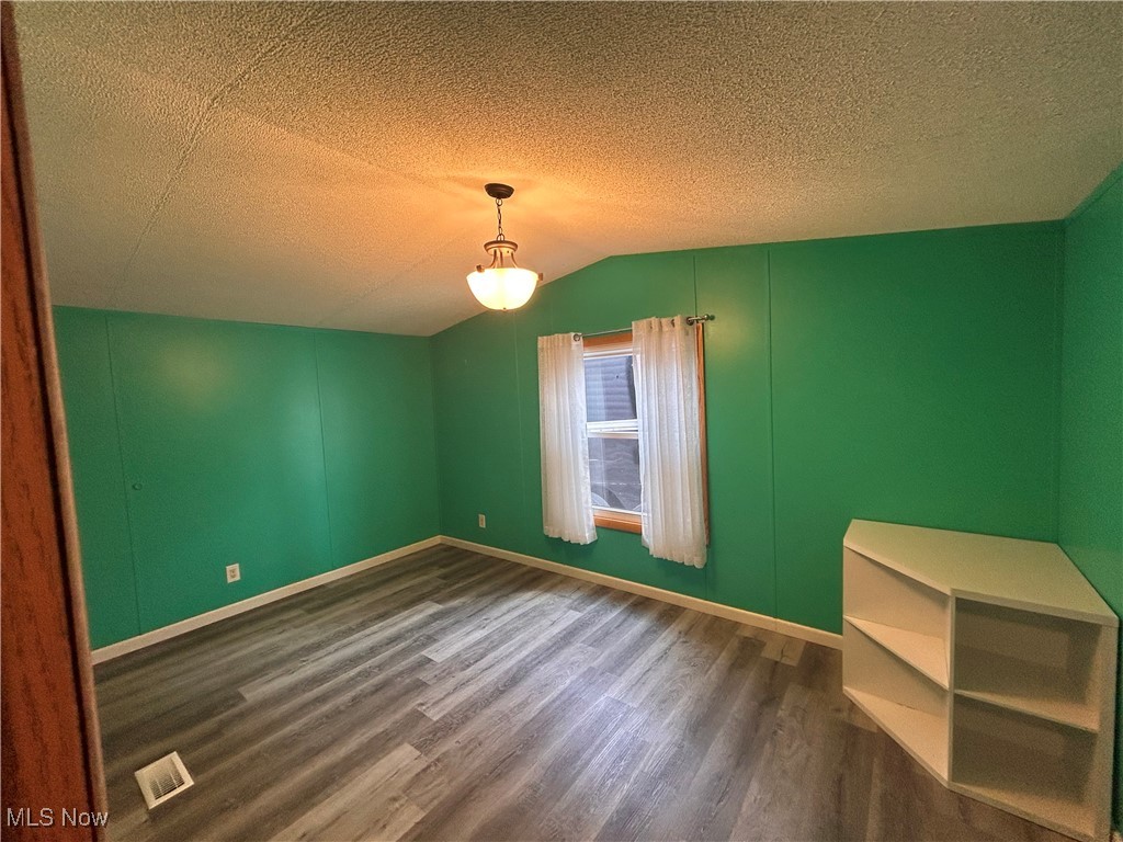 78790 Hamilton Ridge Road Freeport, OH 43973 - Photo 9 of 17 Spare room featuring visible vents, a textured ceiling, wood finished floors, baseboards, and vaulted ceiling