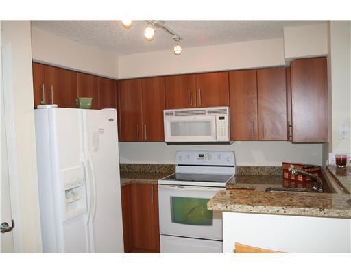 1335 Crystal Way, Unit J Delray Beach, FL 33444 - Photo 3 of 6 a kitchen with stainless steel appliances granite countertop a refrigerator a stove and a sink with wooden cabinets