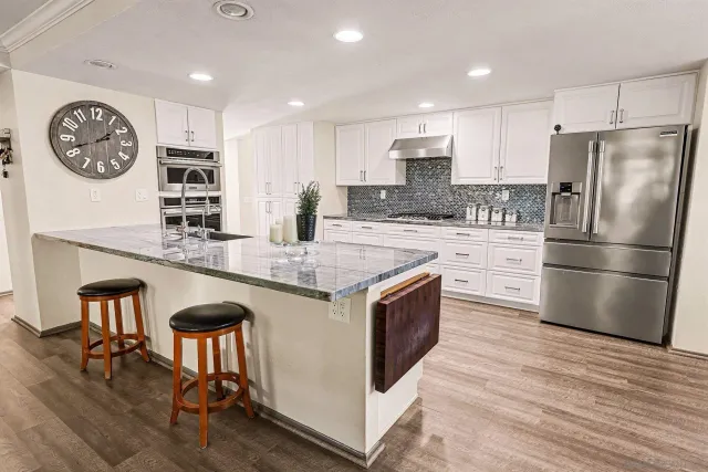 a kitchen with granite countertop a refrigerator a stove a sink and a dining table with wooden floor