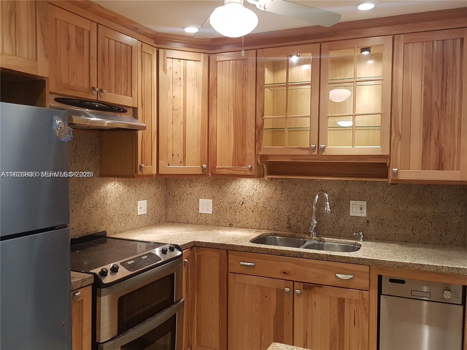 253 South Cypress Road, Unit 237 Pompano Beach, FL 33060 - Photo 2 of 23 a kitchen with granite countertop a stove a sink and dishwasher wooden cabinets