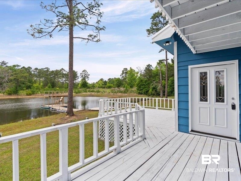 3160 Old Castleberry Road Brewton, AL 36426 - Photo 22 of 36 Expansive wooden deck with white railing, overlooking a pond with a dock, featuring a blue exterior wall with white trim and a white door with decorative glass inserts