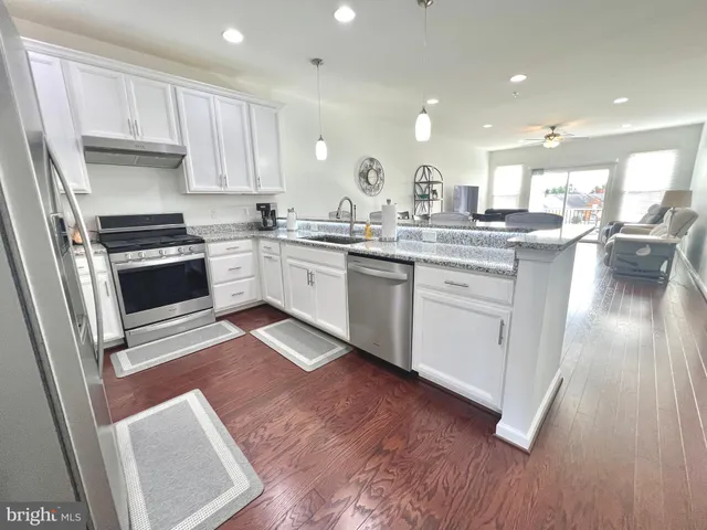 a kitchen with a sink dishwasher stove and white cabinets with wooden floor