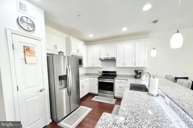 a kitchen with stainless steel appliances granite countertop a refrigerator a stove and a sink with wooden floor