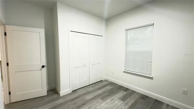 an empty room with wooden floor closet and windows