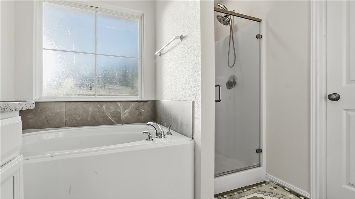 2707 Redcap Street Bryan, TX 77803 - Photo 20 of 28 Soaking tub with polished chrome fixtures and a tiled surround, alongside a glass-enclosed shower with a handheld showerhead