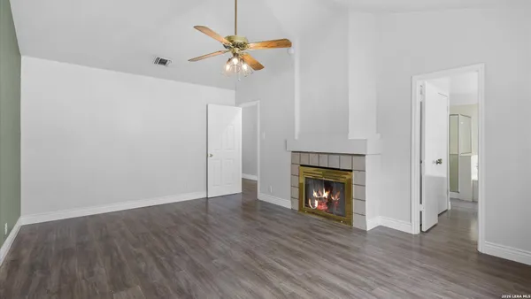 a view of an empty room with wooden floor fireplace and a window