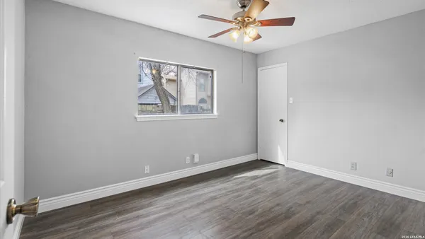 an empty room with wooden floor chandelier fan and windows