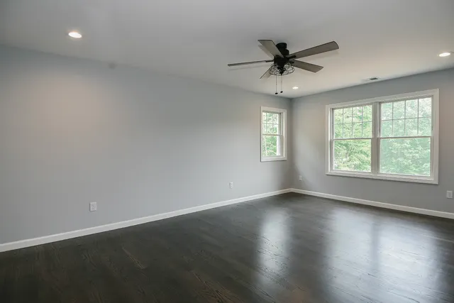 an empty room with wooden floor windows and fan