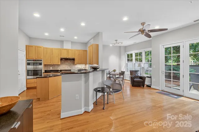 a kitchen with stainless steel appliances kitchen island granite countertop a refrigerator a stove a sink dishwasher with a dining table and chairs with wooden floor