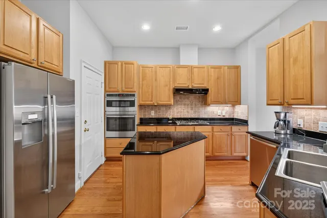 a kitchen with stainless steel appliances granite countertop a refrigerator a sink dishwasher a stove and white countertops with wooden floor