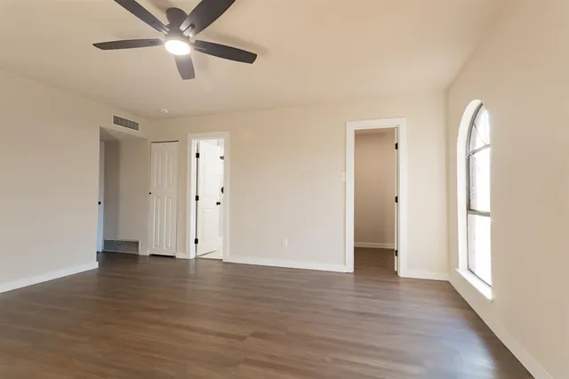 an empty room with wooden floor chandelier fan and windows