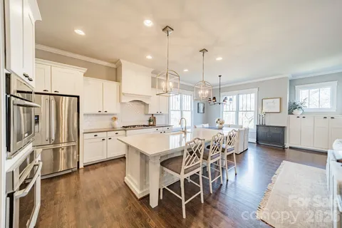 a kitchen with stainless steel appliances kitchen island granite countertop a refrigerator a stove a sink a dining table and chairs with wooden floor