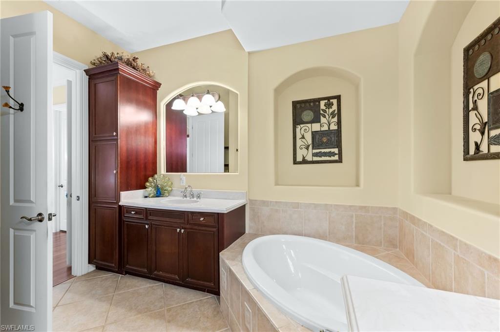 7875 Valencia Court Naples, FL 34113 - Photo 20 of 38 Bathroom featuring vanity, a garden tub, and light tile patterned floors