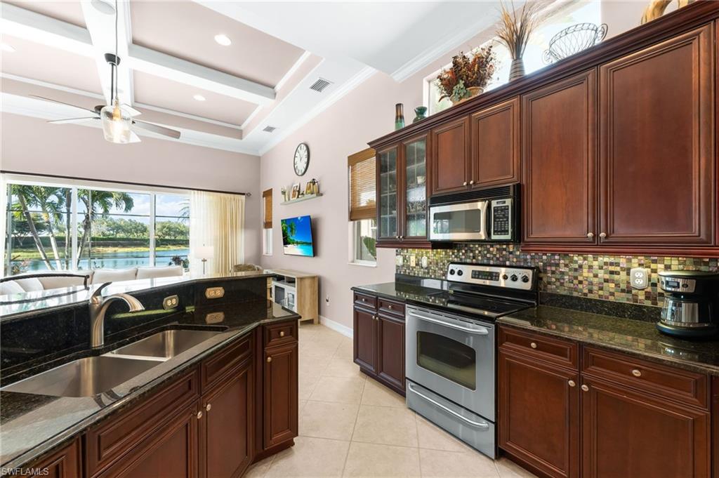 7875 Valencia Court Naples, FL 34113 - Photo 8 of 38 Kitchen with stainless steel appliances, granite counters, coffered ceiling, glass fronted cabinets, and a ceiling fan