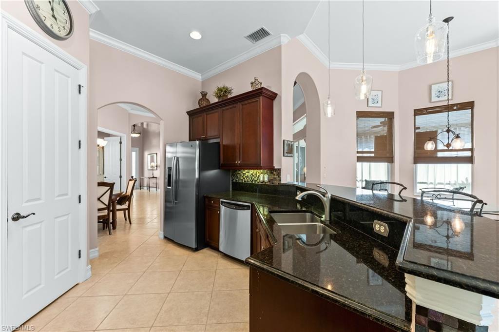 7875 Valencia Court Naples, FL 34113 - Photo 9 of 38 Kitchen featuring granite countertops, arched walkways, decorative light fixtures, light tile patterned floors, and ornamental molding