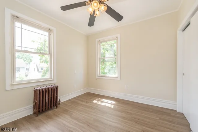 an empty room with wooden floor chandelier fan and windows